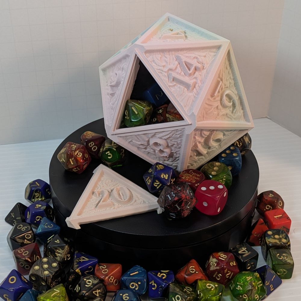 A 3D printed dice container shaped like a d20. It's printed in a matte pastel filament, heavy on the pink tones. The 20 is removed, showing dice inside the container.