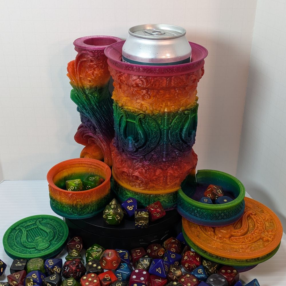 A "tankard" that acts as a dice tower, dice vault, and can holder. It's in a bright rainbow gradient, and it's disassembled to show the dice tower in the handle, the can in the main cavity, the small dice vault at the side, and the screw-on lid.