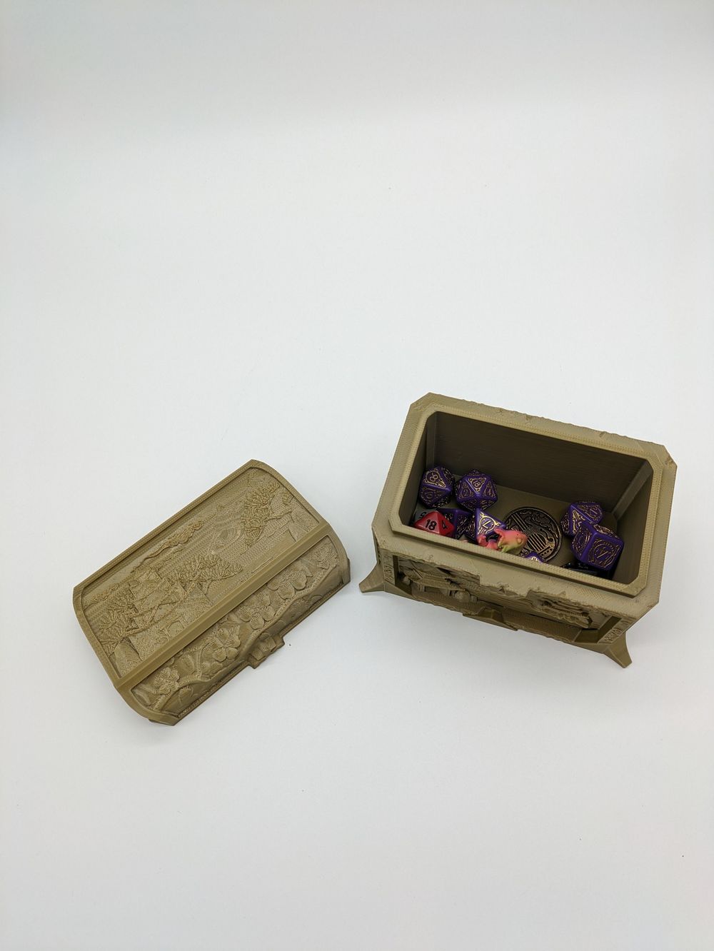 A shot from above over a golden colored 3d printed dice box. The lid is removed from the box, showing a set of dice and a few other trinkets inside. 