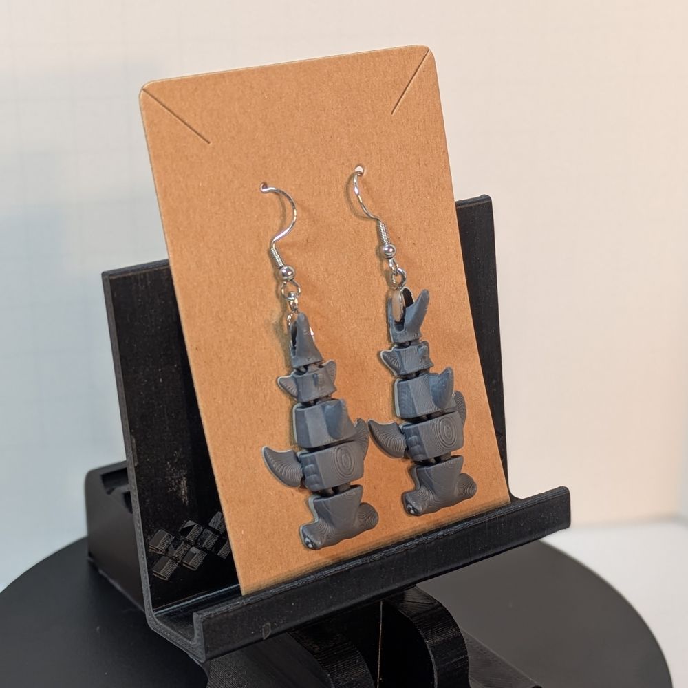 A pair of grey 3d printed hammerhead sharks hanging on a brown cardboard earring card.