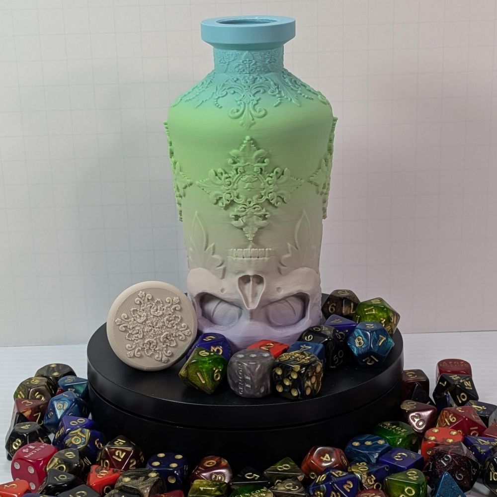 A 3D printed bottle with decorative work around it. The base is shaped like an upside down skull. It's printed in a light pastel gradient filament, and it's surrounded by many colorful dice.
